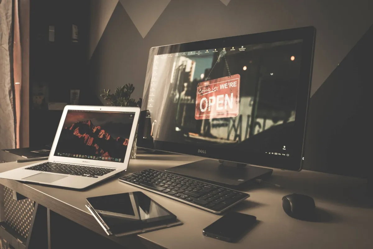 Desk with a laptop, desktop monitor, keyboard, tablet and phone